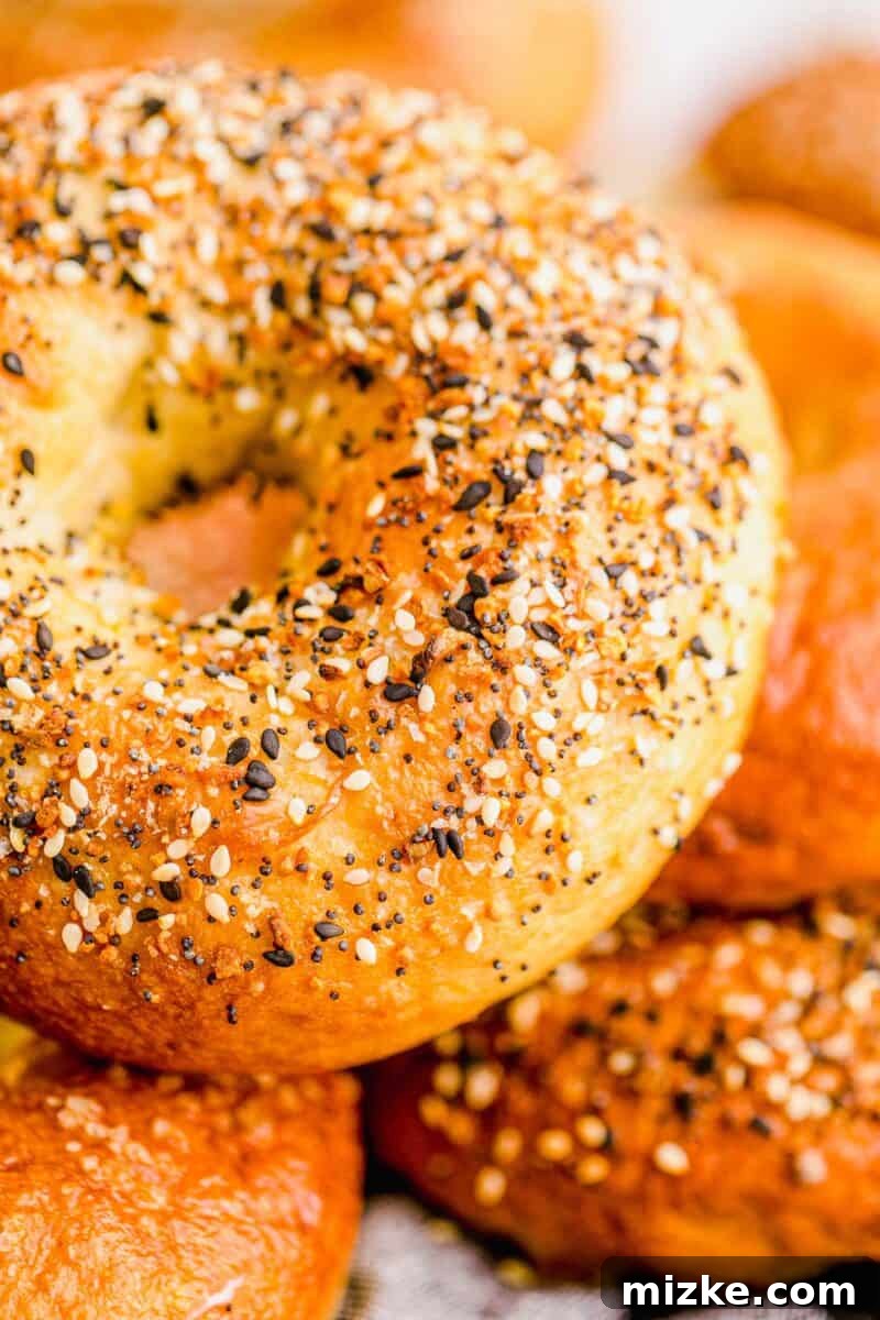 Chewy Homemade Bagels From Scratch 17 A single sesame seed bagel perfectly placed on top of a stack of other freshly baked, golden-brown bagels.