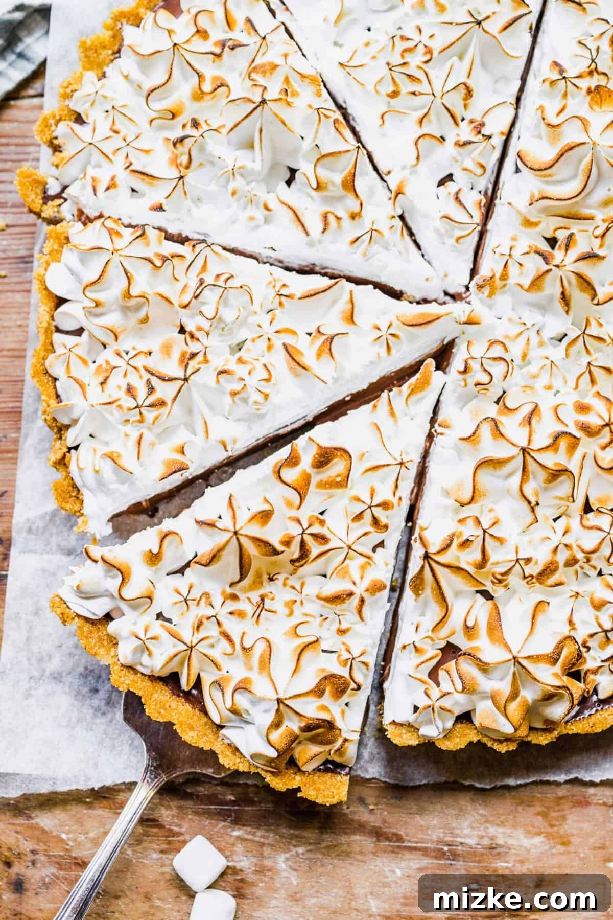 This s'mores tart recipe takes just 15 minutes to make! With a graham cracker crust, ganache filling, and toasty meringue, it's irresistible. Overhead view of sliced s'mores tart showcasing its layers