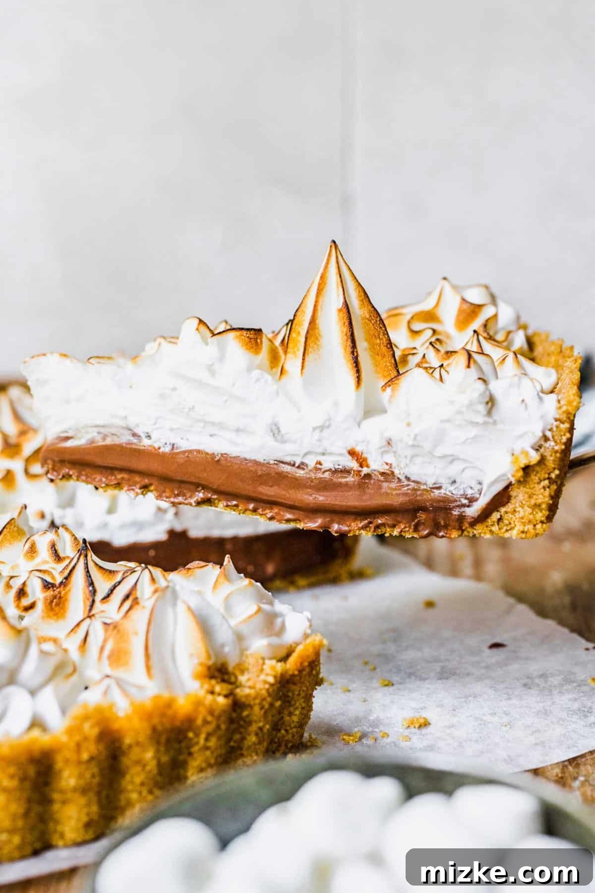 This s'mores tart recipe takes just 15 minutes to make! With a graham cracker crust, ganache filling, and toasty meringue, it's irresistible. A slice being removed from a freshly made s'mores tart