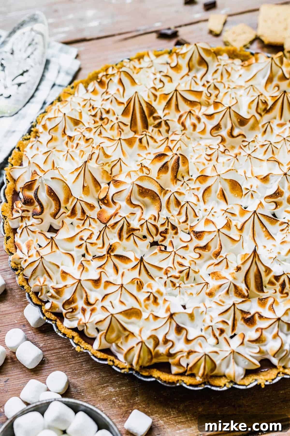 This s'mores tart recipe takes just 15 minutes to make! With a graham cracker crust, ganache filling, and toasty meringue, it's irresistible. Whole s'mores tart resting in a tart pan before serving
