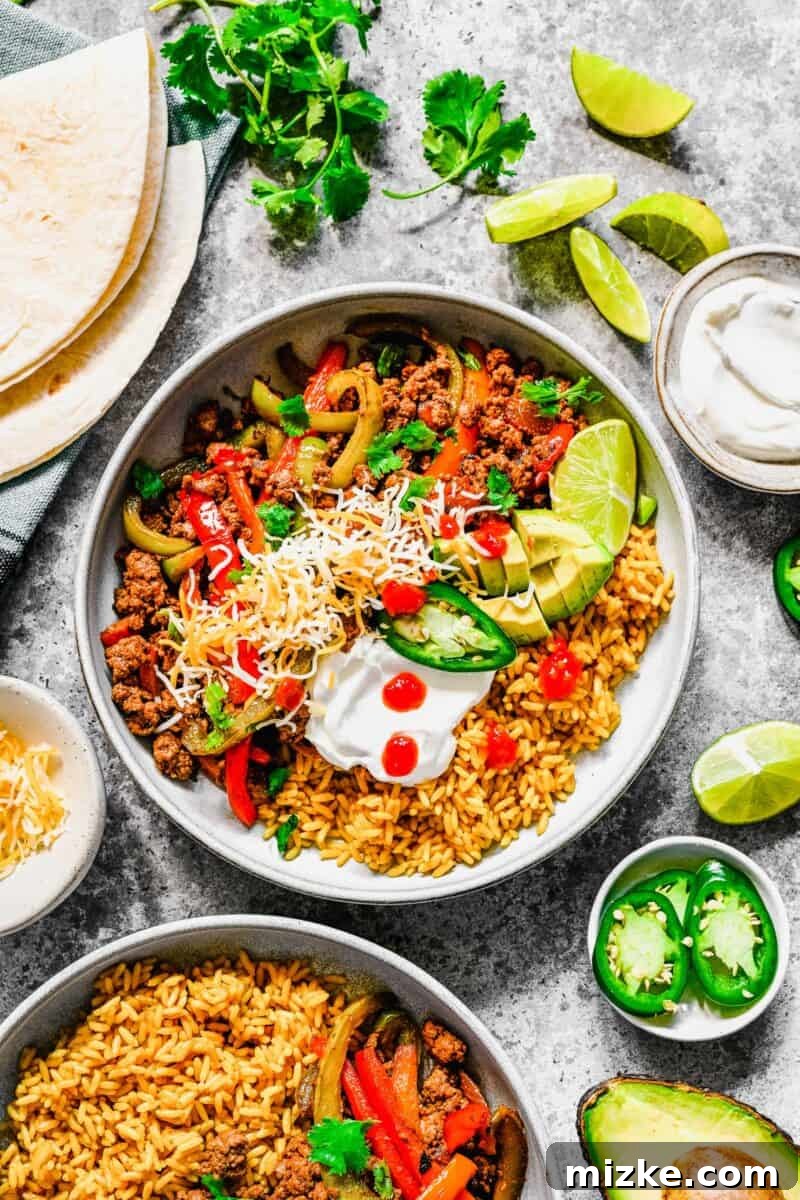 Sizzling Ground Beef Fajitas 2 A white bowl is filled with ground beef fajitas, rice, and several toppings, showcasing a complete meal.