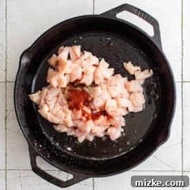 cubed chicken and seasonings in a cast iron skillet