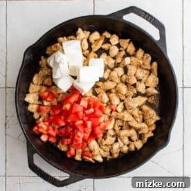 tomatoes, cream cheese, and cooked chicken in a cast iron skillet