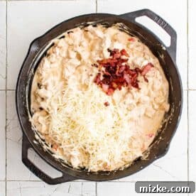 shredded mozzarella cheese and bacon pieces on top of cooked chicken mixture in cast iron skillet