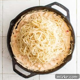 cooked spaghetti has been added to a cast iron skillet