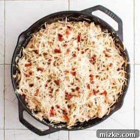 mozzarella cheese and more bacon is topped on chicken spaghetti in a cast iron skillet