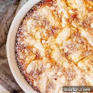A golden brown Apple Almond Coffee Cake sits on a white plate. It is topped with almond slices and finished with powdered sugar.