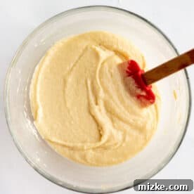 batter for apple almond cake in a clear bowl with a red silicone spatula