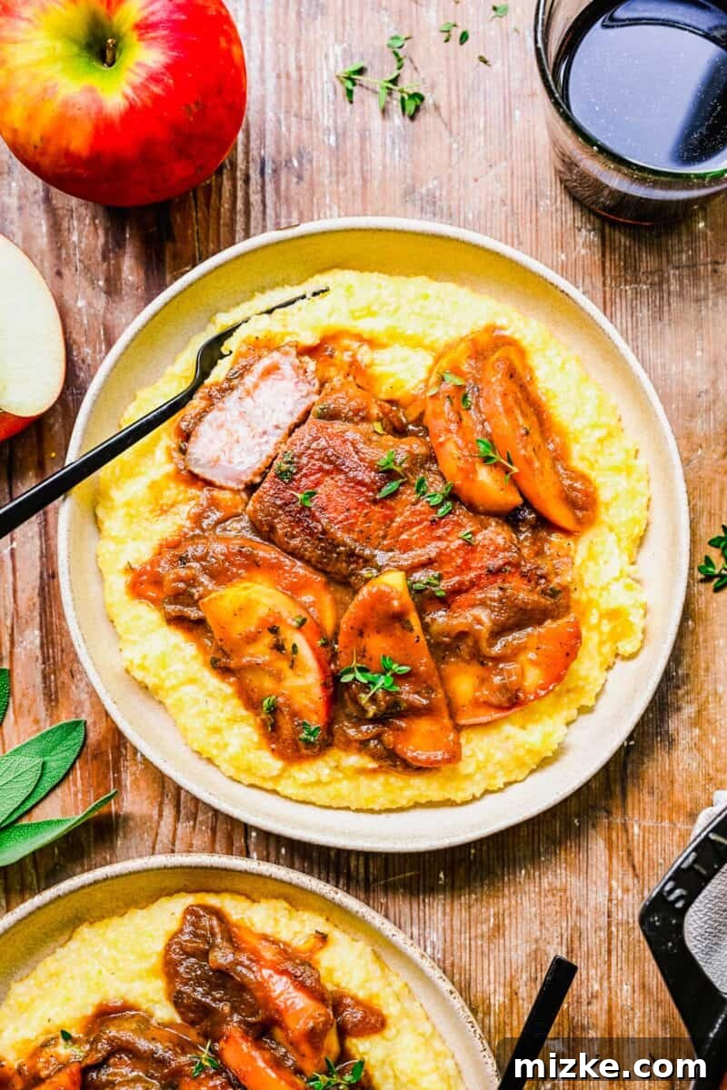 Spiced Apple Butter Pork Chops 2 Apple butter pork chops are presented on top of cooked polenta on a white plate.