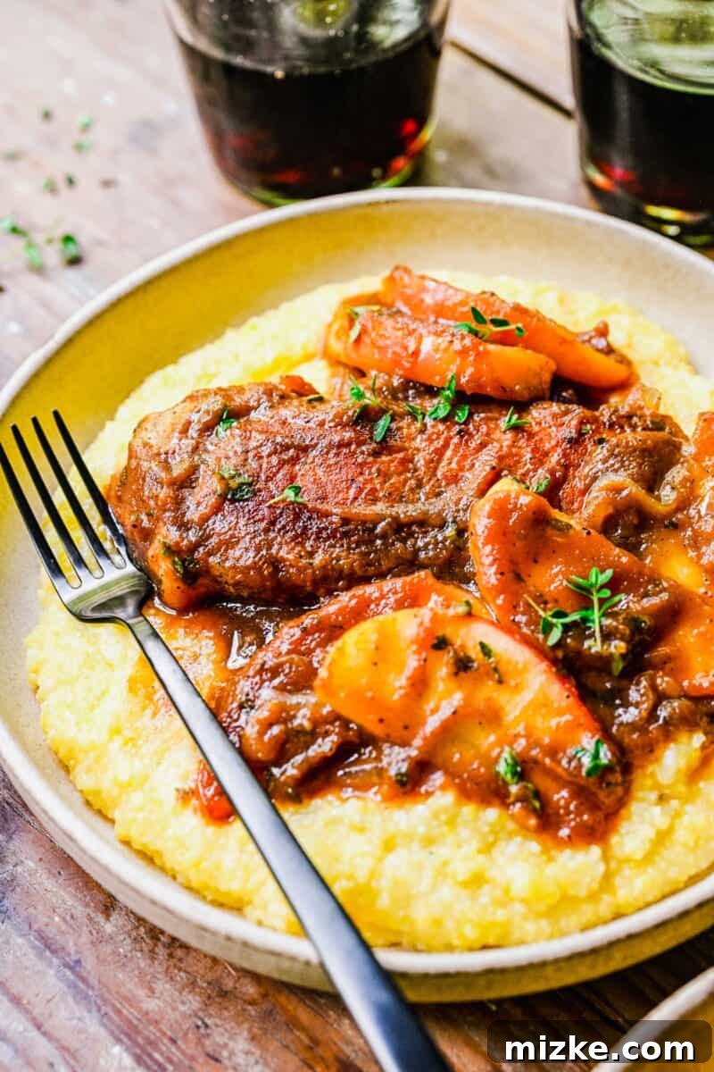 Spiced Apple Butter Pork Chops 5 A fork is placed on a round white plate filled with apple butter pork chops and polenta.