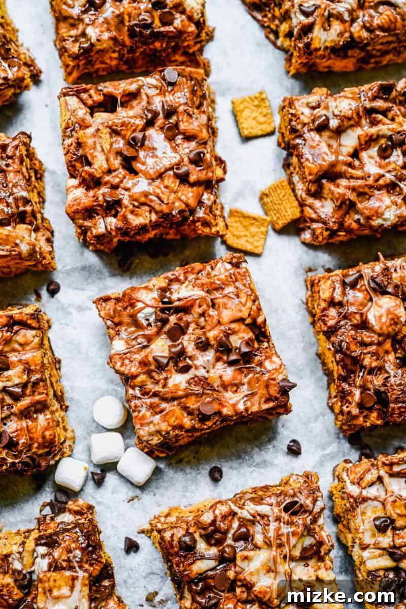 Ultimate Golden Grahams Smores Treat 2 Perfectly portioned Golden Grahams S'mores Bars are placed next to each other on a rustic surface, with extra mini marshmallows and chocolate chips scattered invitingly around them.