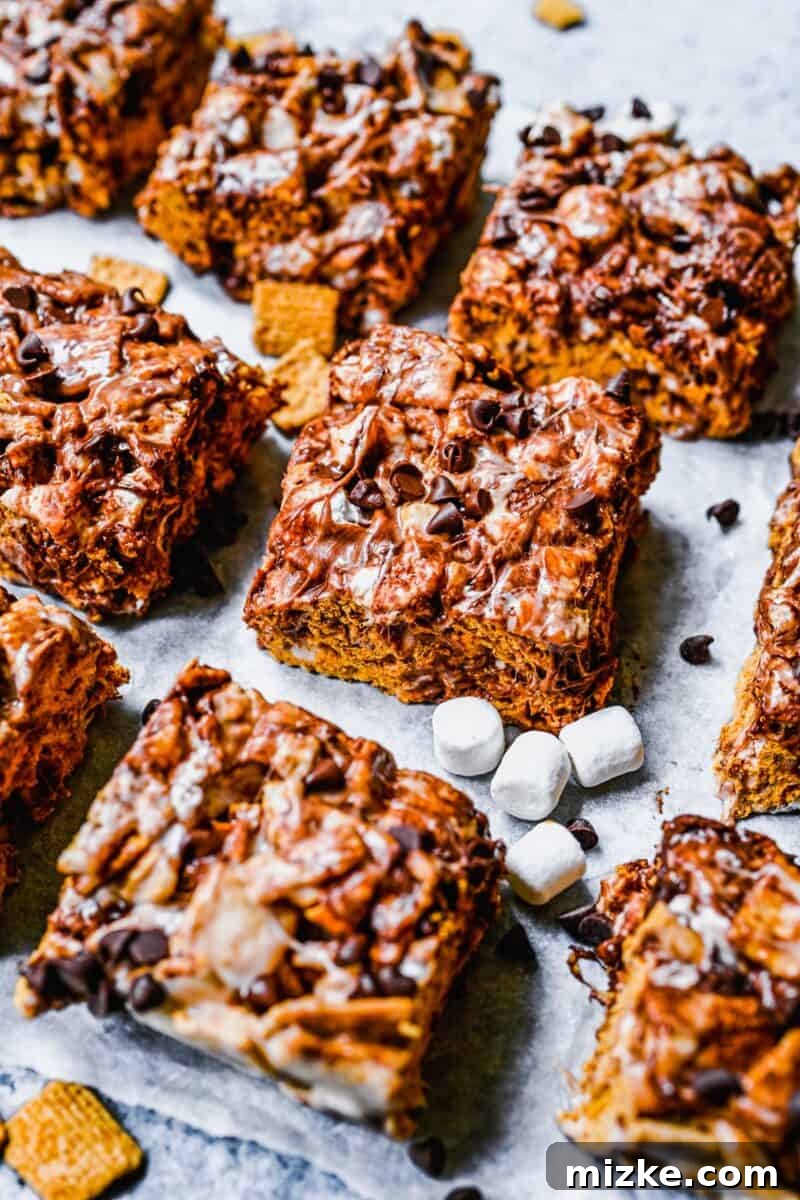 Ultimate Golden Grahams Smores Treat 3 Soft, white mini marshmallows and rich, dark mini chocolate chips are scattered around perfectly sliced Golden Grahams S'mores Bars, highlighting the key ingredients.