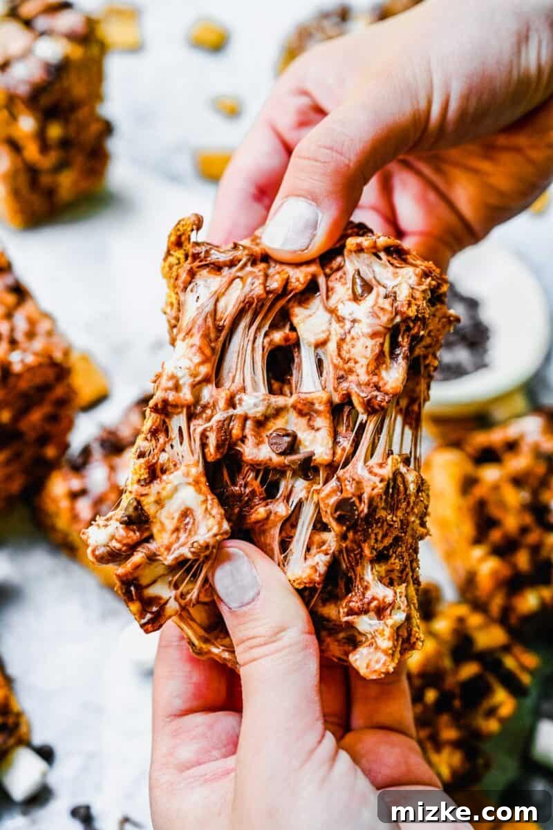 Ultimate Golden Grahams Smores Treat 5 Hands are gently pulling apart a soft and gooey Golden Grahams S'mores Bar, revealing its stretchy marshmallow and chocolate layers.