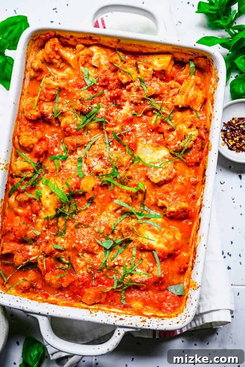 Fresh basil garnishes a baking dish full of delectable baked cauliflower parmesan, enhancing its visual appeal.