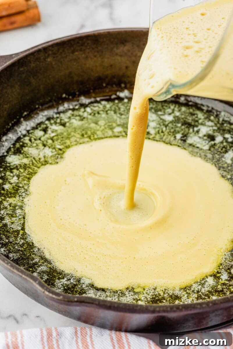 Puffy Apple Cinnamon Dutch Baby 6 Smooth Dutch Baby batter is gently poured into the hot, buttered cast-iron skillet, creating the foundation for the puffed pancake.