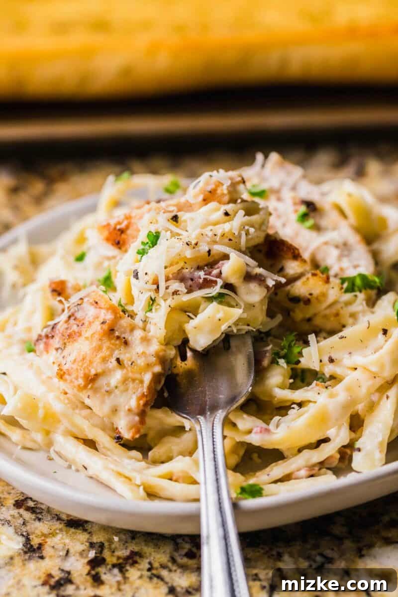 Creamy Garlic Parmesan Chicken Pasta 12 A fork is piercing a bite sized portion of chicken and pasta on a plate.