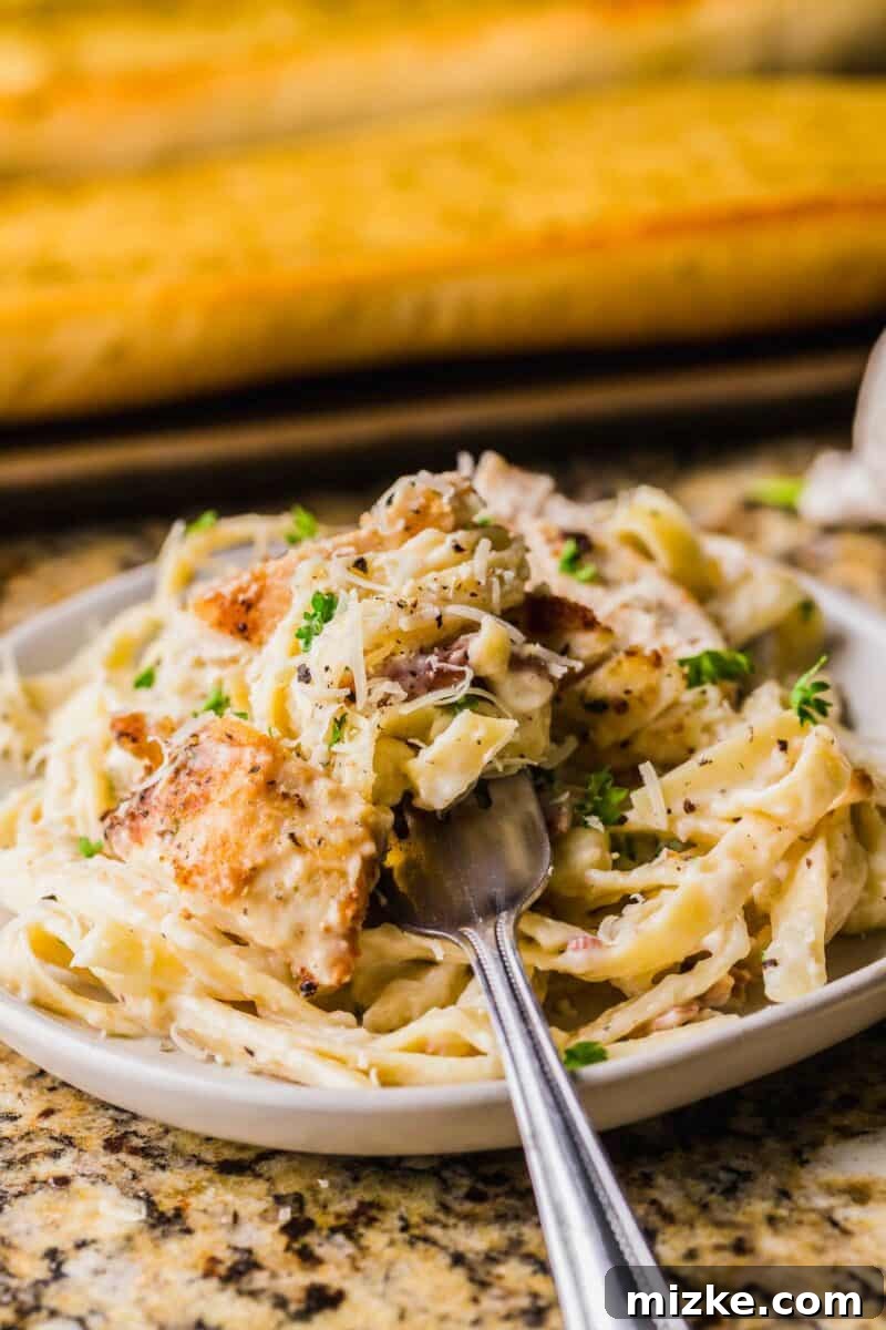 Creamy Garlic Parmesan Chicken Pasta 4 A fork is placed on a white plate filled with chicken and pasta.