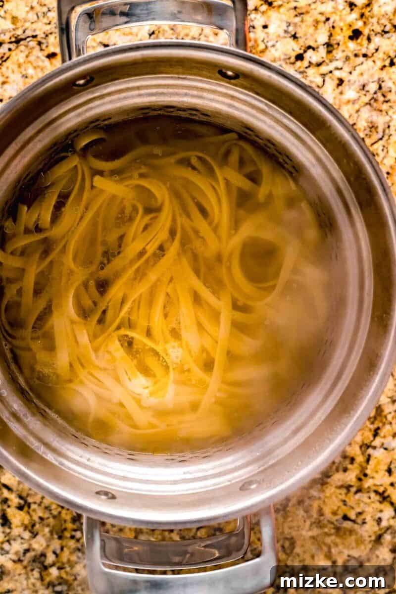 Creamy Garlic Parmesan Chicken Pasta 6 fettuccine noodles being cooked in a stainless steel pot with water