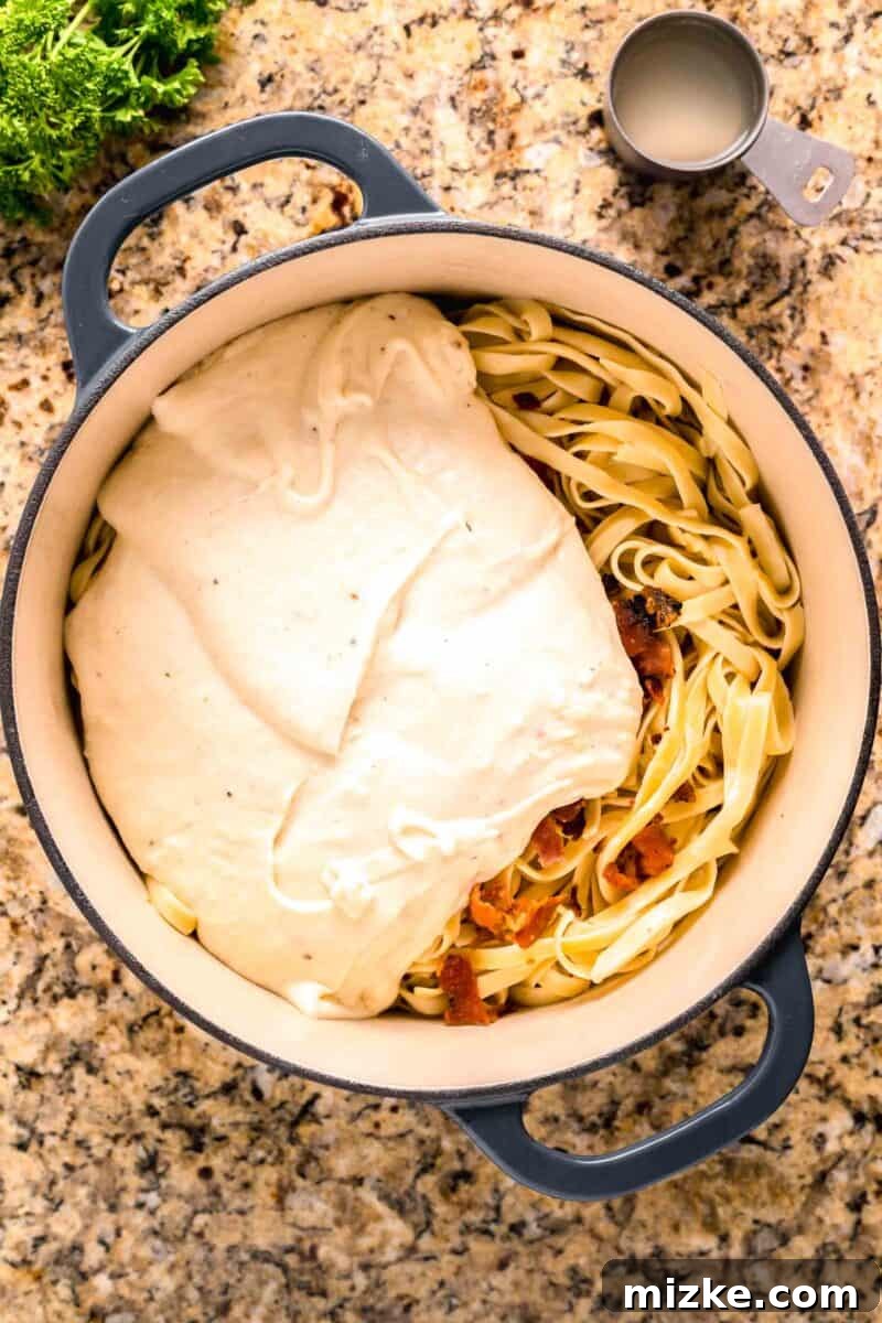 Creamy Garlic Parmesan Chicken Pasta 9 cream sauce poured on top of pasta and bacon in a blue dutch oven