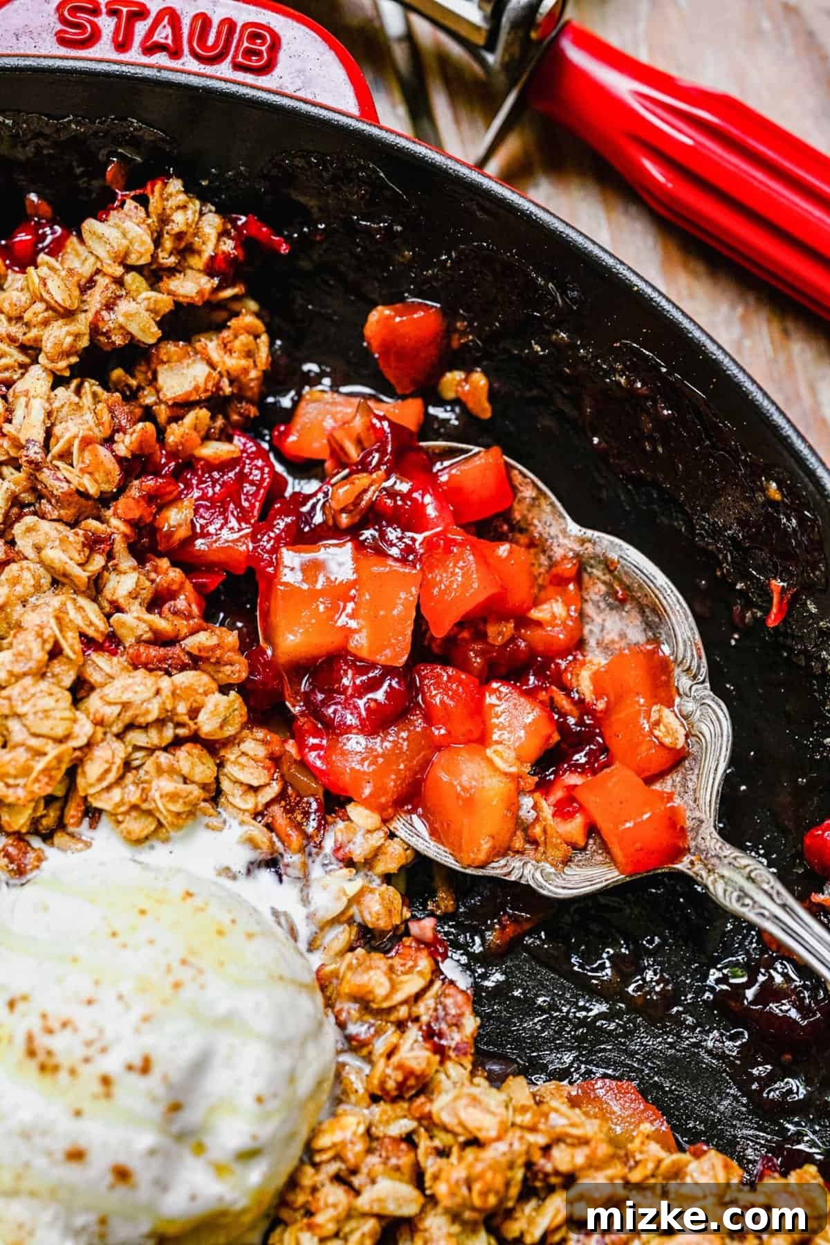A warm scoop of Apple Cranberry Crisp, a perfect addition to any dessert spread. A silver serving spoon scoops a generous portion of warm apple cranberry crisp from a pan, revealing the fruit filling and crispy topping.