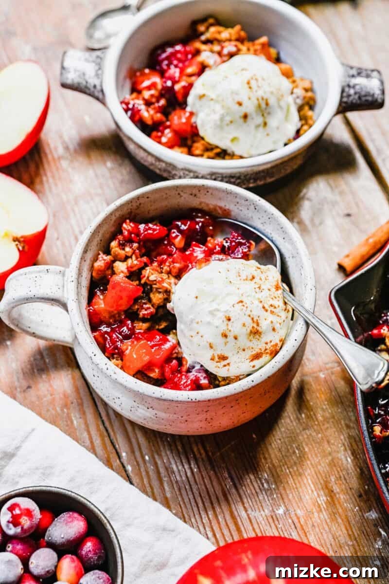 Sweet & Tart Cranberry Apple Crisp 2 Multiple servings of apple cranberry crisp with ice cream, arranged in white mugs on a warm wooden background, ready to be enjoyed.