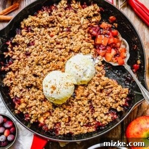 A pan of apple cranberry crisp with a silver serving spoon sitting atop, ready to be served.