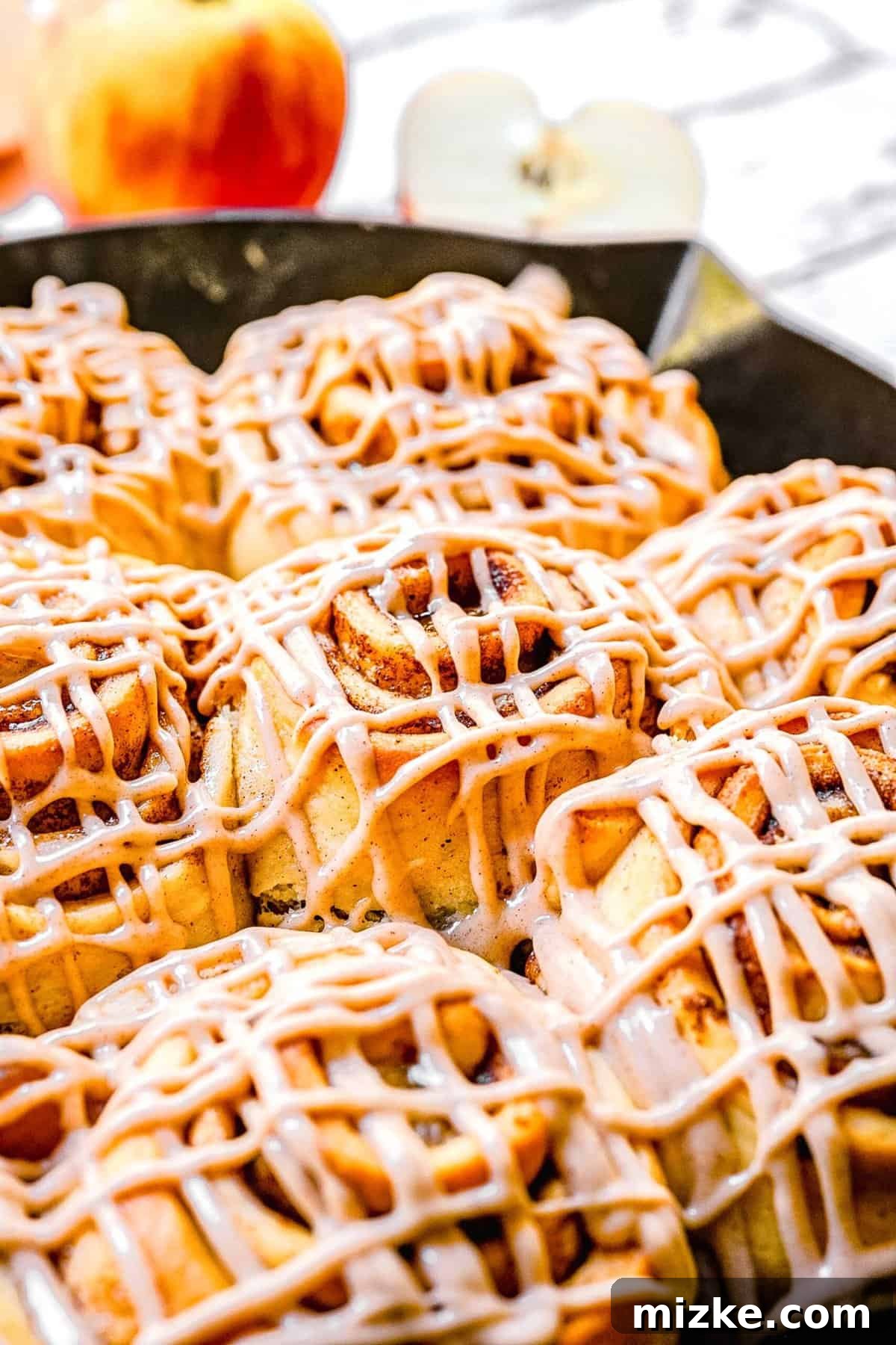 A stunning close-up of generously frosted apple pie cinnamon rolls, showcasing their tender texture and delicious topping.