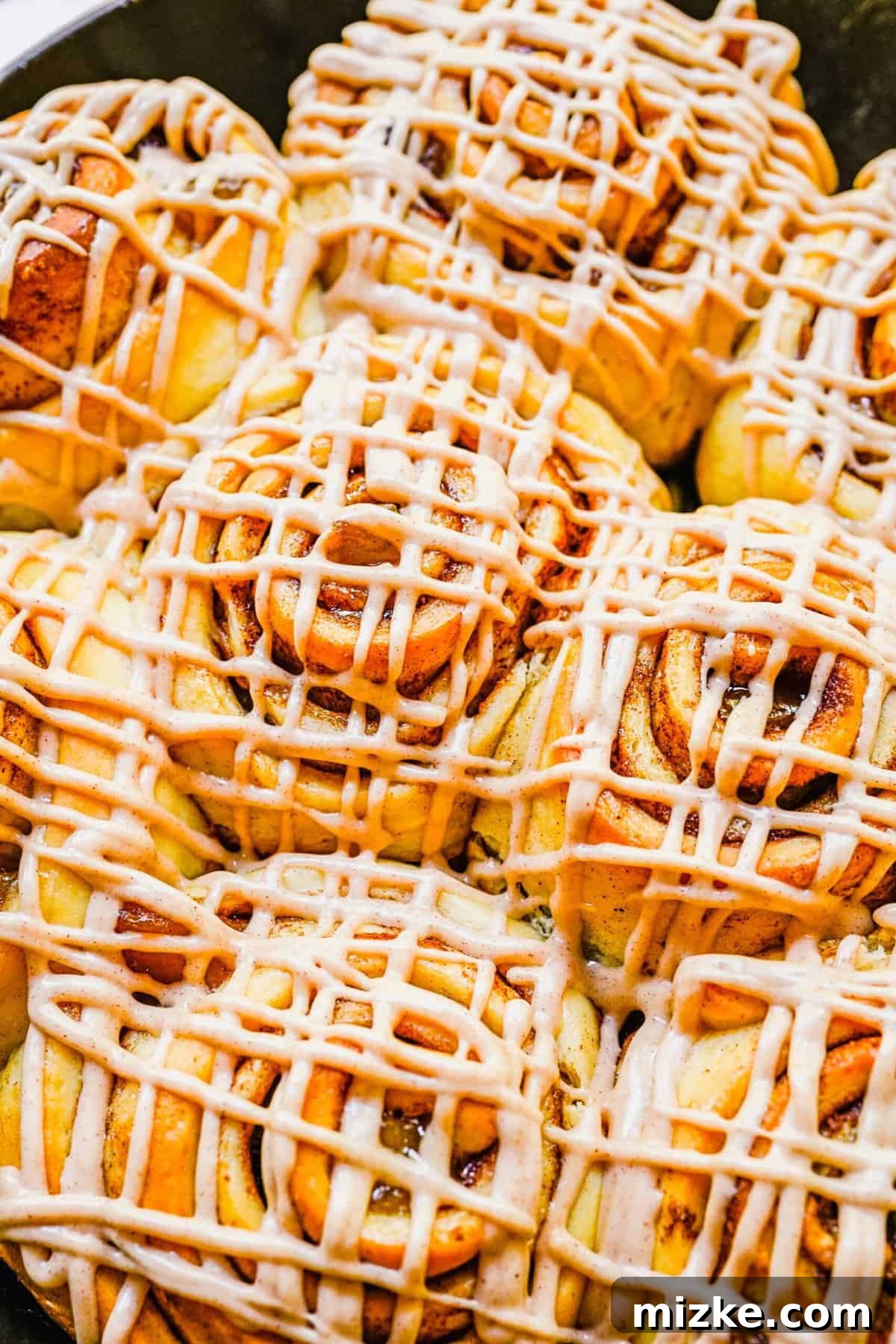 A delightful array of apple pie cinnamon rolls, each generously covered with luscious cream cheese frosting, presented in a baking dish.
