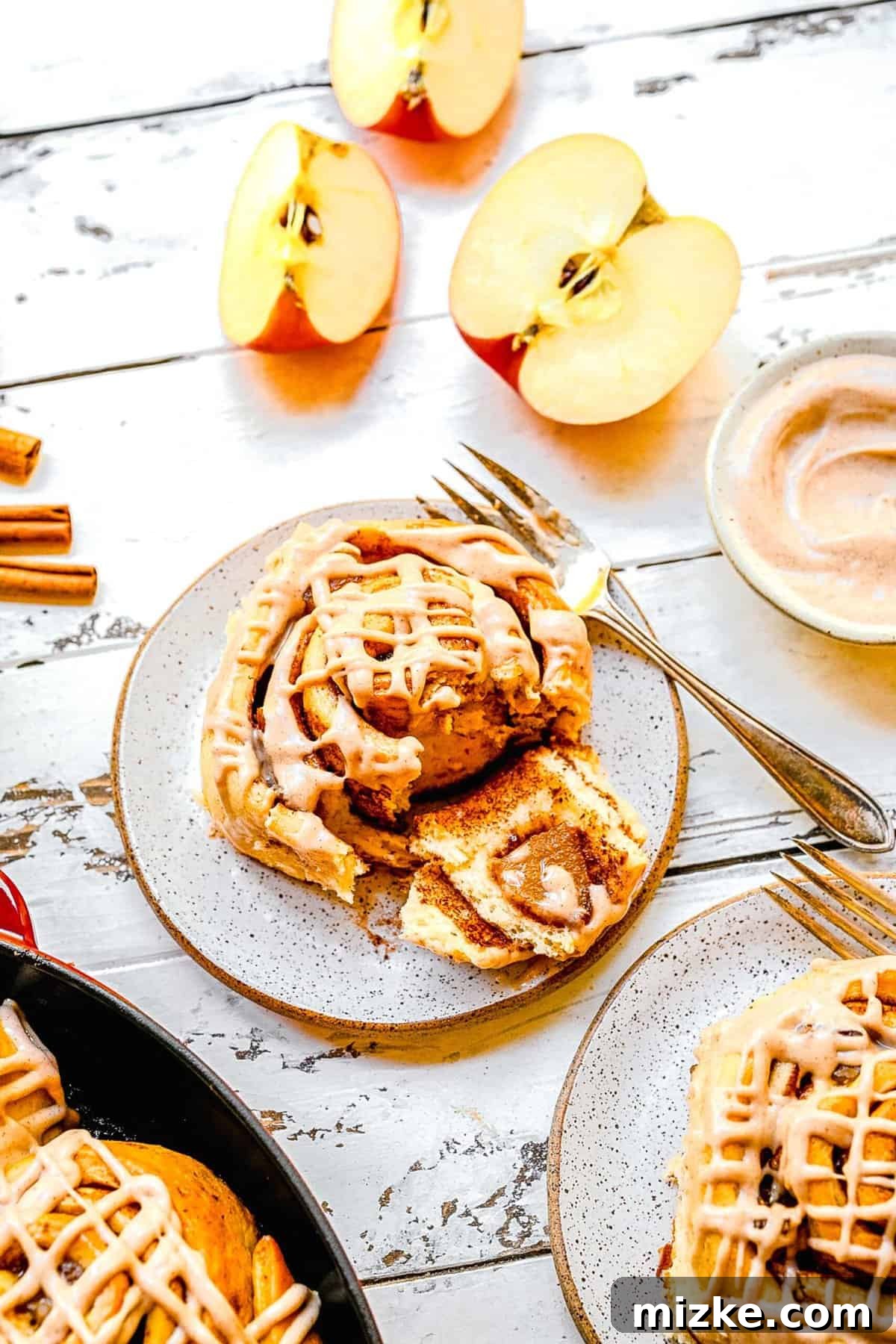 A single, delectable apple pie cinnamon roll artfully plated on a white-washed wooden table, ready to be enjoyed.