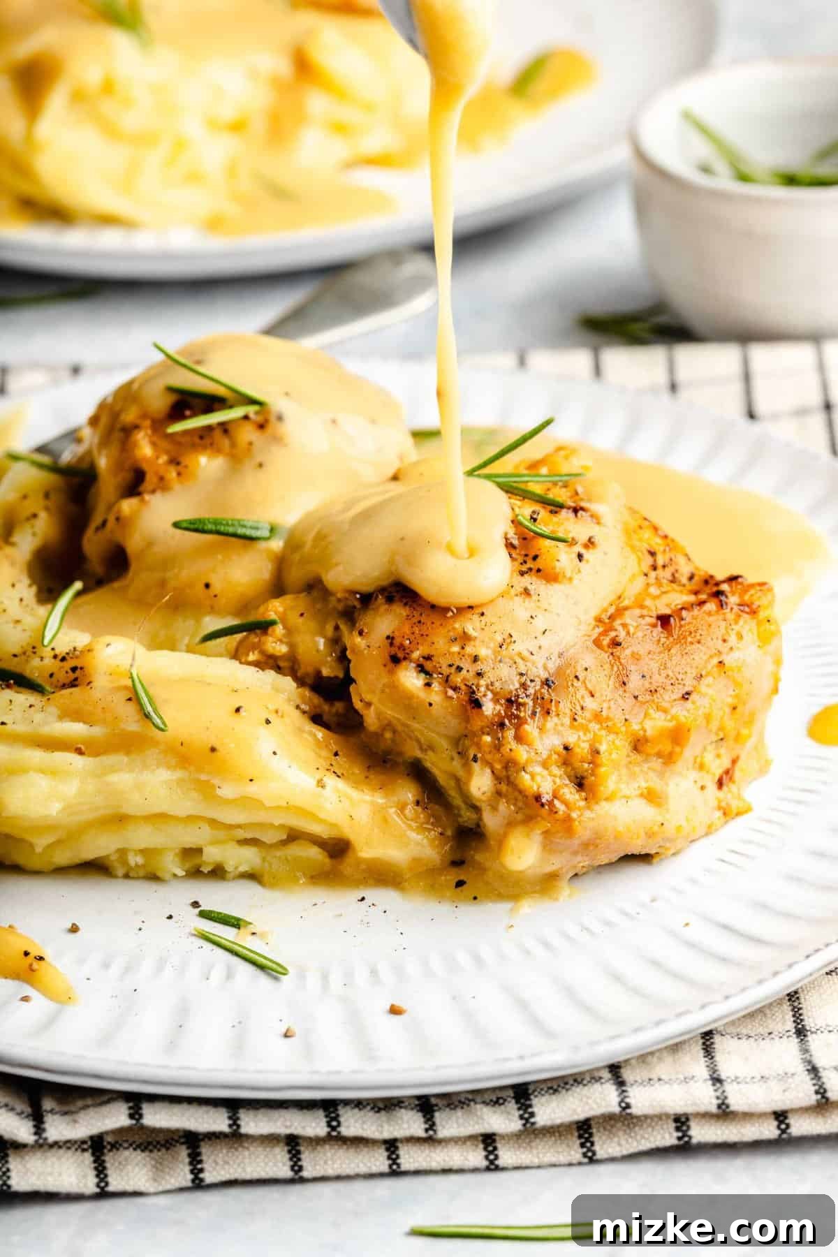 Easy Maple Dijon Yum Yum Chicken: Tender chicken thighs smothered in a savory-sweet Dijon mustard & maple syrup sauce. Pouring sauce over yum yum chicken in a baking dish.