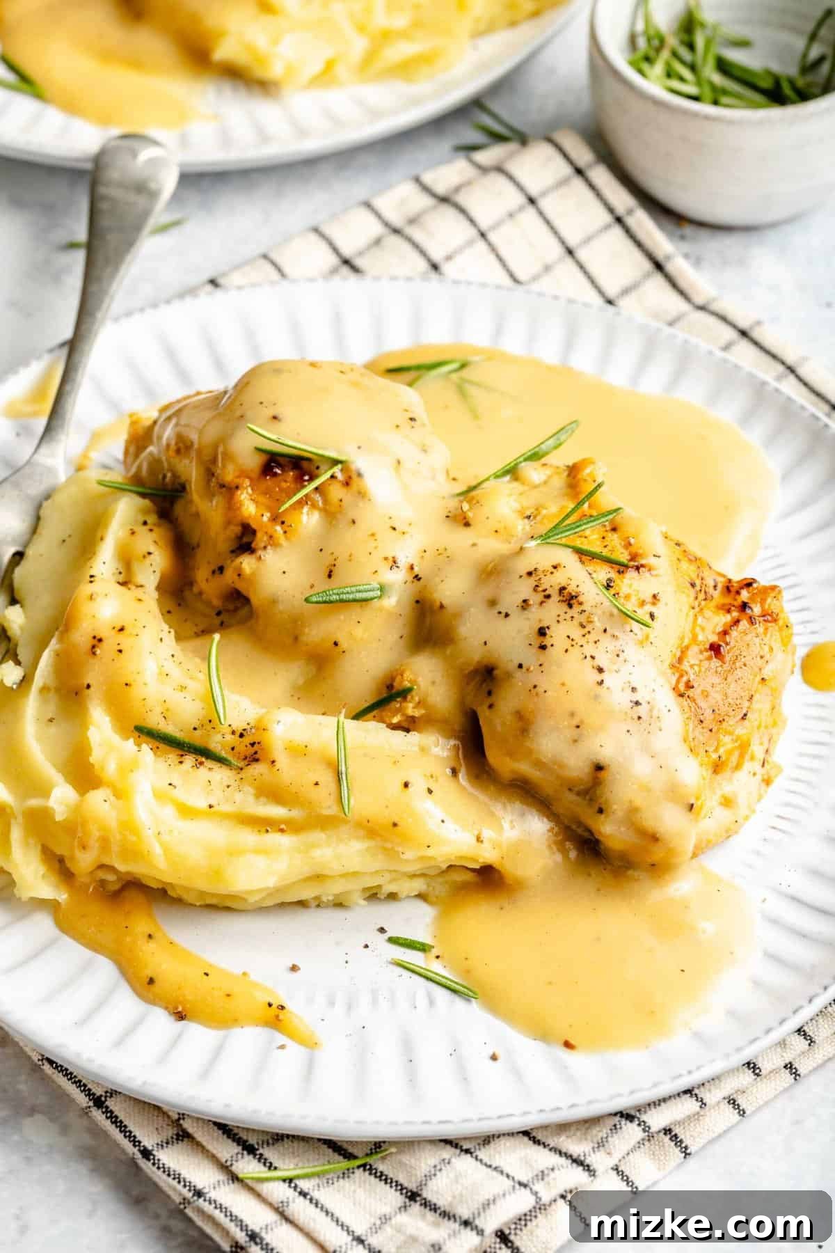 A perfectly cooked plate of easy Maple Dijon Yum Yum Chicken with rich sauce and fresh rosemary. Plate of Maple Dijon Yum Yum Chicken garnished with rosemary.