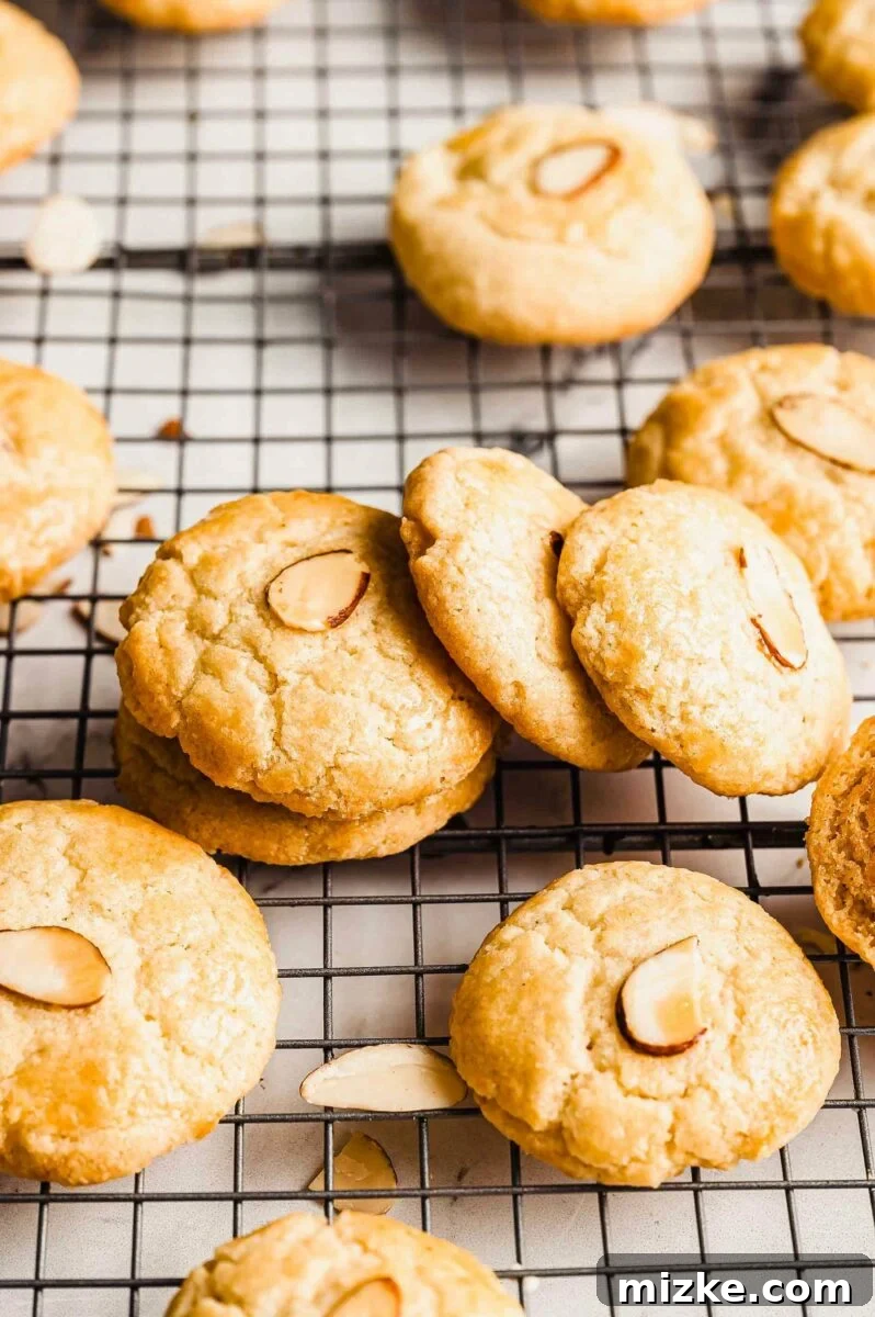 Chinese almond cookies cooling on a metal rack, showcasing their circular coin shape and perfectly placed sliced almond.