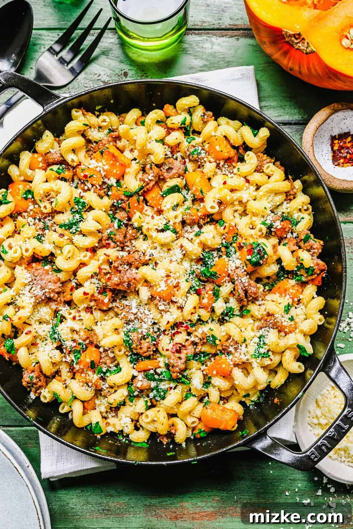 Creamy Pumpkin Sausage Pasta 2 Overhead shot of finished pumpkin sausage pasta in a rustic cast iron pot, garnished with grated Parmesan cheese and red pepper flakes.