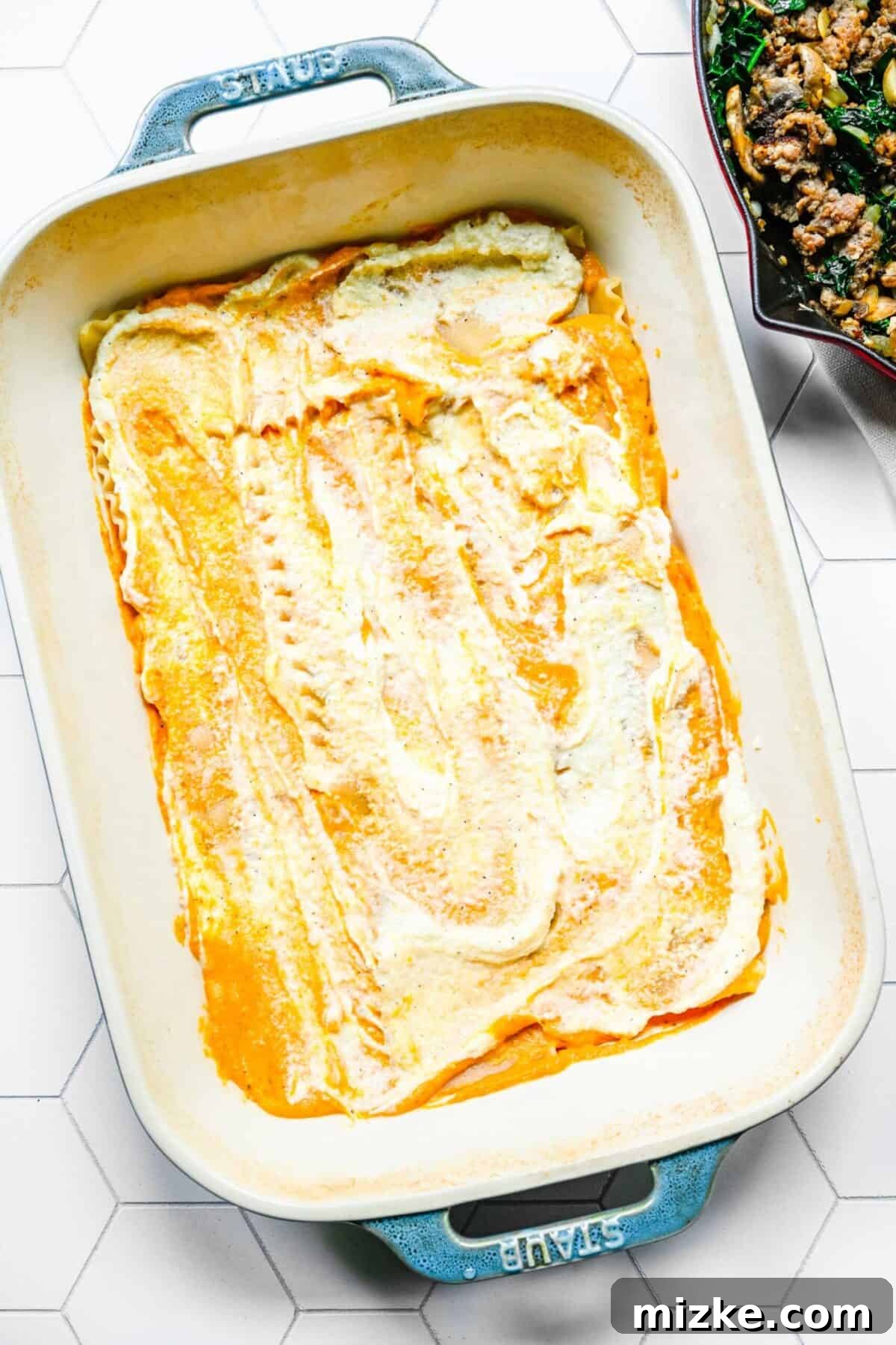 First layers of pumpkin sauce and ricotta filling in the baking dish A baking dish with pumpkin cream sauce and ricotta filling spread over a layer of lasagna noodles, showcasing the initial layers