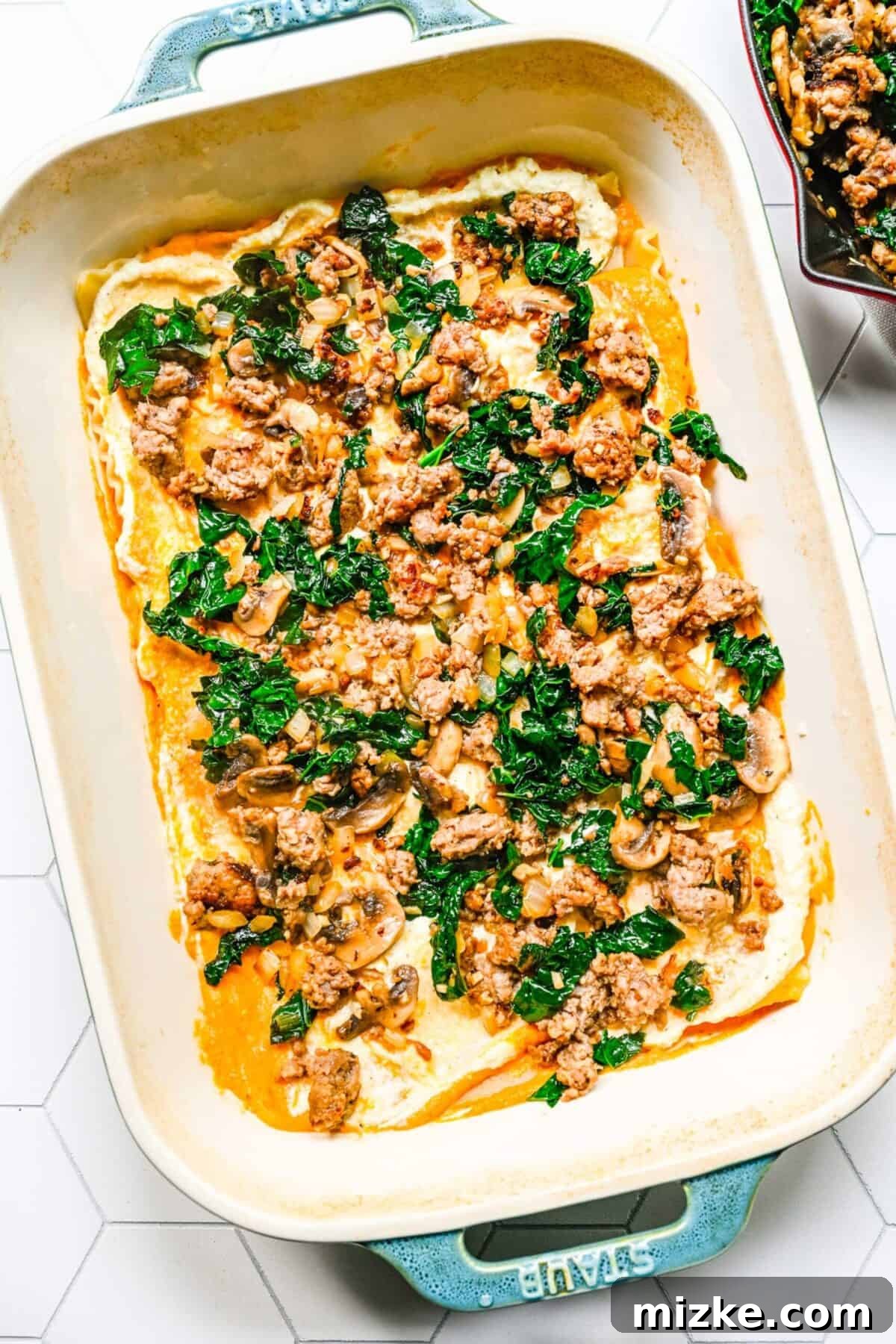 Sausage and kale mixture spread over the ricotta layer A baking dish with cooked sausage and kale spread over pumpkin cream sauce and ricotta filling, on top of lasagna noodles, showing a completed layer