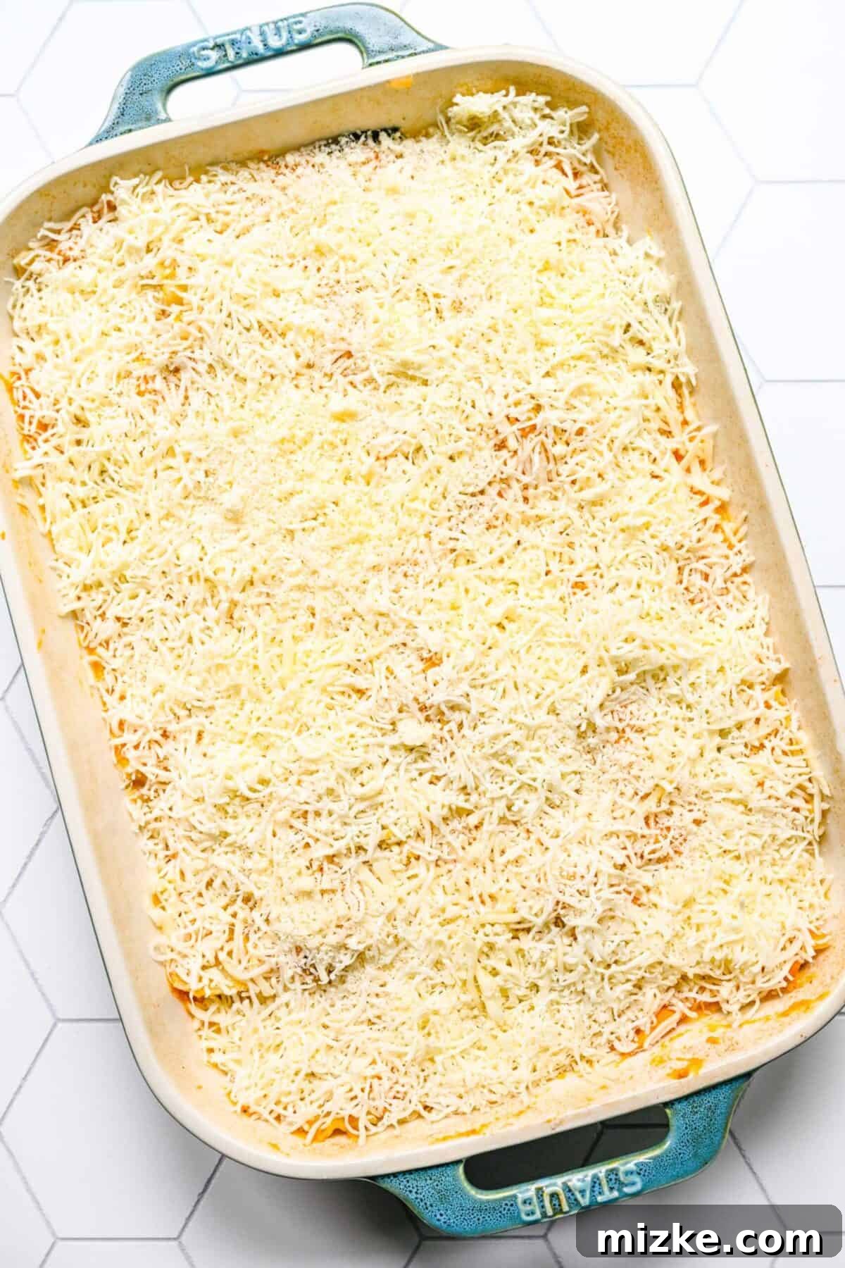 Unbaked pumpkin lasagna, generously topped with cheese A baking dish filled with an uncooked pumpkin lasagna, generously topped with shredded mozzarella and parmesan cheese