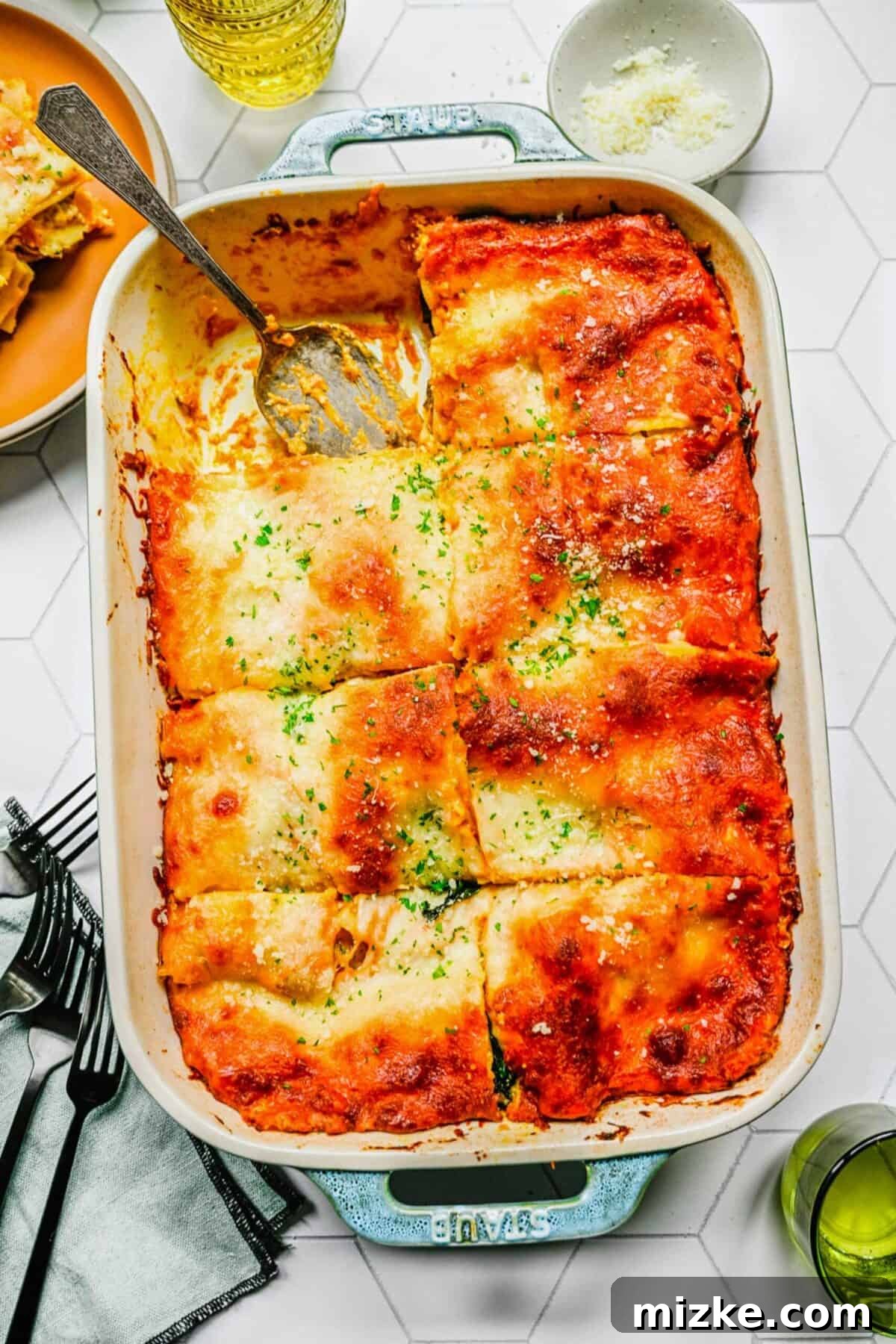 Baked pumpkin lasagna, sliced and ready to enjoy A baking tray with pumpkin lasagna cut into eight slices, with one slice removed and a serving spoon in it, ready to serve