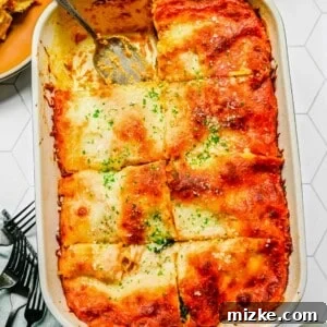 A baking tray with pumpkin lasagna cut into eight slices, with one slice removed and a serving spoon in it