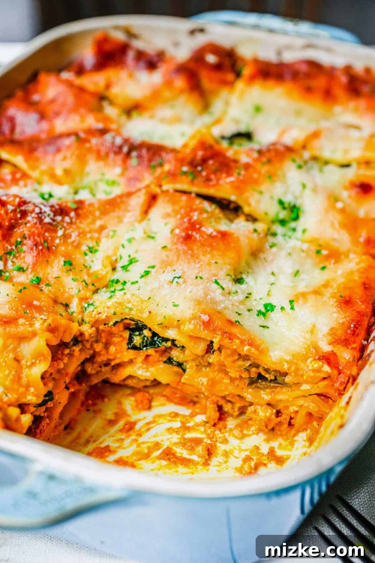 Hearty and Flavorful Pumpkin Lasagna with Sausage and Kale - Perfect for a Cozy Meal Close up of the corner of a baking tray with pumpkin lasagna, with the corner piece removed, showing off the perfectly cooked layers
