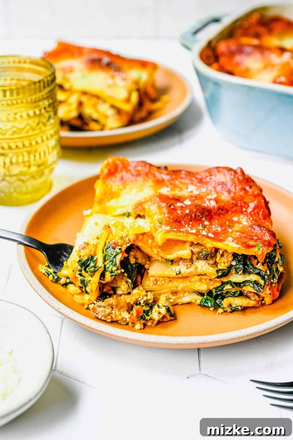 Indulgent Pumpkin Lasagna with Sausage and Kale - A Gourmet Comfort Dish A plate with a slice of pumpkin lasagna, with a fork taking a forkful of it, with another plate of lasagna in the background, showcasing its delicious texture