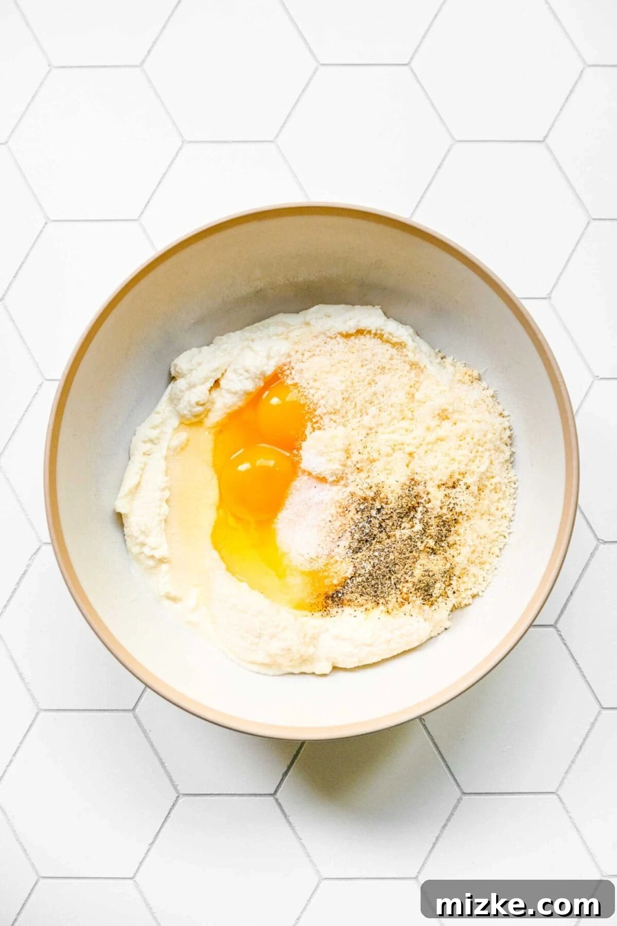 Ingredients for the creamy ricotta filling, pre-mixing A mixing bowl filled with unmixed ricotta, grated parmesan, eggs, salt, pepper, and garlic powder