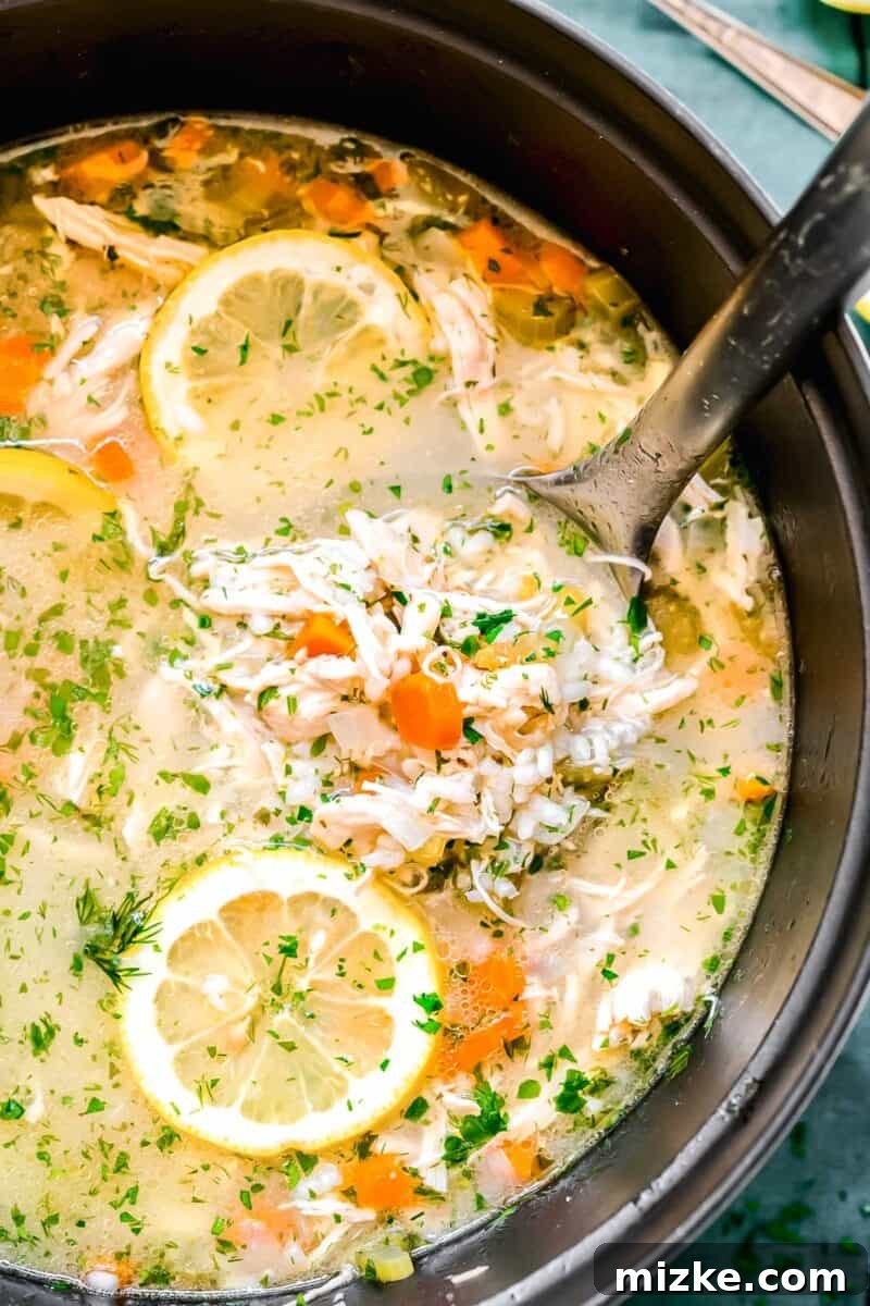 Zesty Lemon Chicken Rice Soup 3 Close-up shot of creamy lemon chicken and rice soup in a ladle, gently scooped from a large pot, surrounded by fresh lemon slices