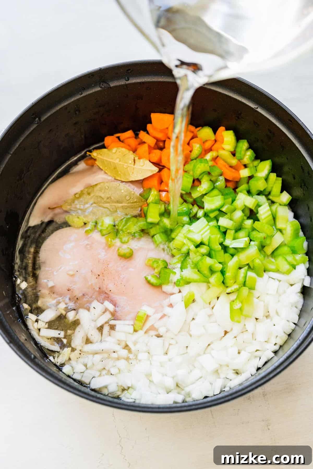 Zesty Lemon Chicken Rice Soup 6 A stream of clear water being poured over raw chicken, bay leaves, and diced vegetables in a large pot