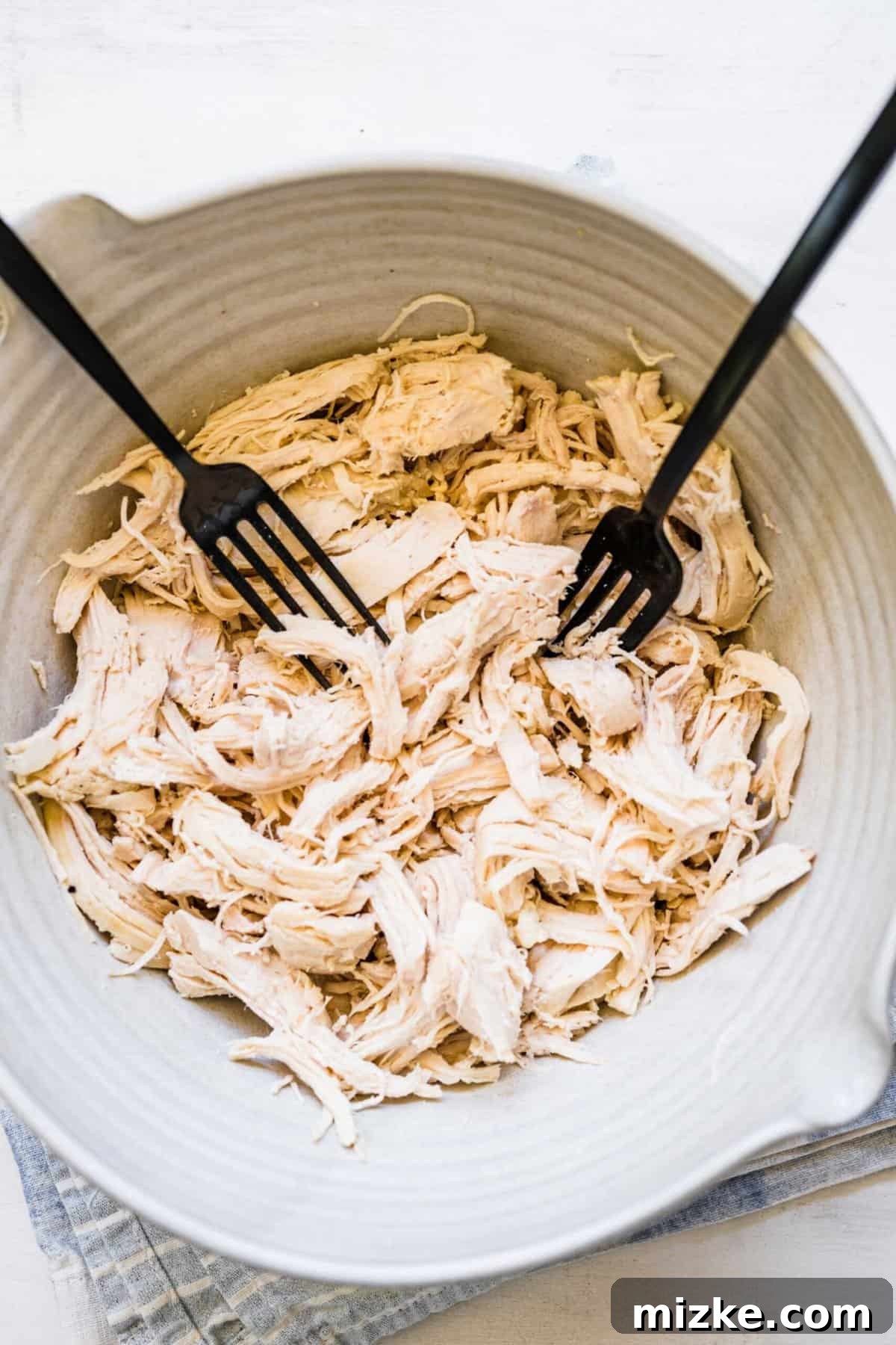 Zesty Lemon Chicken Rice Soup 7 Two black forks pulling apart shredded chicken in a large white bowl