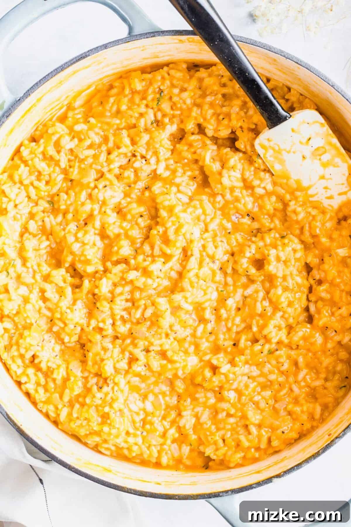 How to make creamy vegan mushroom risotto for a wholesome dinner. A large pot of perfectly cooked vegan mushroom risotto, with a rubber spatula embedded in its creamy texture, ready for serving.