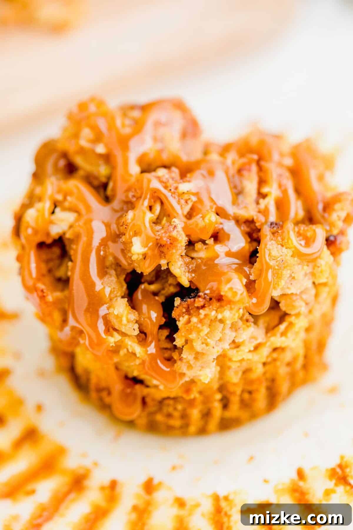 Close-up of a single mini caramel apple cheesecake. A close-up shot focusing on a single, perfectly crafted mini caramel apple cheesecake, showcasing its golden streusel topping, visible apple chunks, and creamy filling, promising a delicious bite.