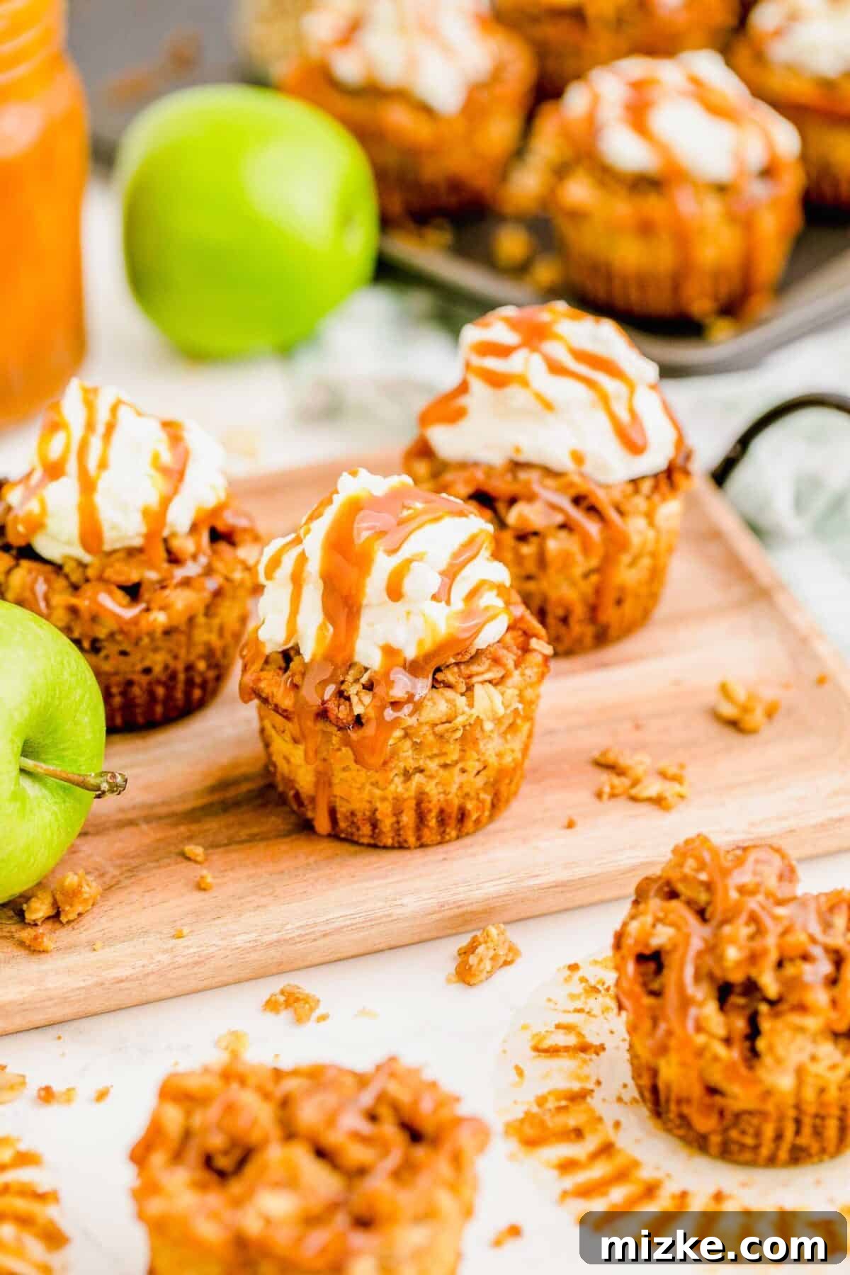 Three mini caramel apple cheesecakes surrounded by fresh apples. A charming overhead view of three mini caramel apple cheesecakes presented on a wooden cutting board, surrounded by fresh, vibrant apples and other delightful cheesecakes in the soft background, creating a rustic and inviting culinary scene.