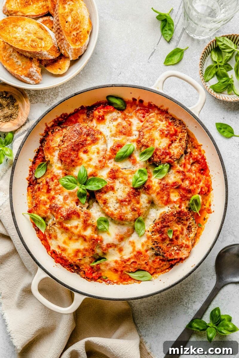 Our all-time FAVORITE way to make crispy eggplant parm! You will want to make it this way forever! #eggplantparm #eggplantparmesan #eggplantrecipe #vegetarian #recipe #italian An overhead shot of a perfectly baked eggplant parmesan in a round casserole dish, ready to be served.