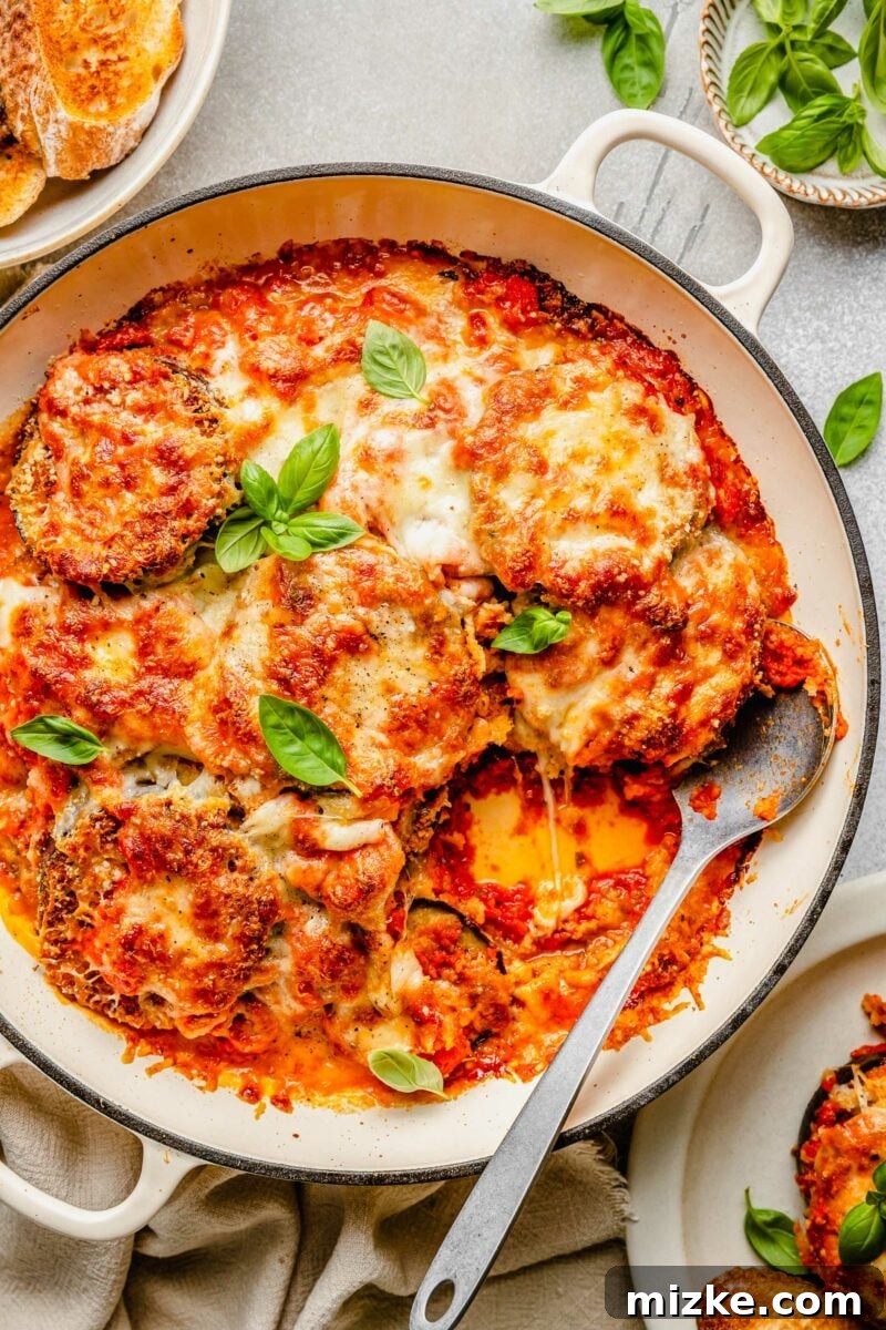 Our all-time FAVORITE way to make crispy eggplant parm! You will want to make it this way forever! #eggplantparm #eggplantparmesan #eggplantrecipe #vegetarian #recipe #italian Overhead view of an eggplant parmesan casserole in a round baking dish with one serving already removed, showing the layers.