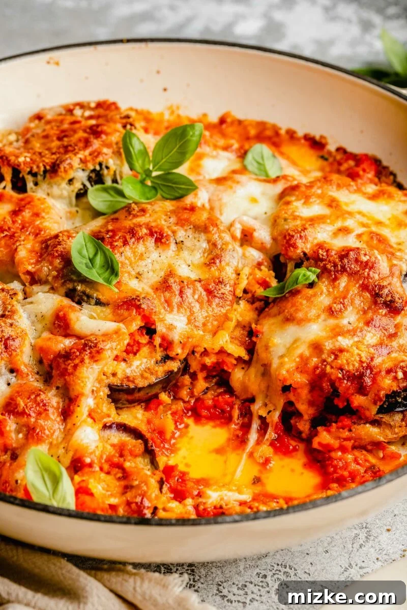 Our all-time FAVORITE way to make crispy eggplant parm! You will want to make it this way forever! #eggplantparm #eggplantparmesan #eggplantrecipe #vegetarian #recipe #italian Close-up shot of baked eggplant parmesan in a round baking dish, highlighting the bubbly tomato sauce and gooey, melted cheese.